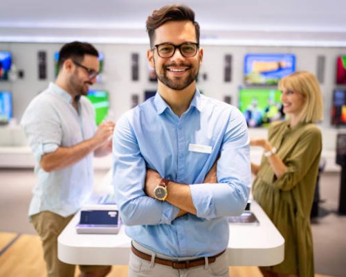 Sales consultant advises people who chooses new digital devices in store of household appliances, electronics and gadgets. Professional consultation in store. Sale Day.